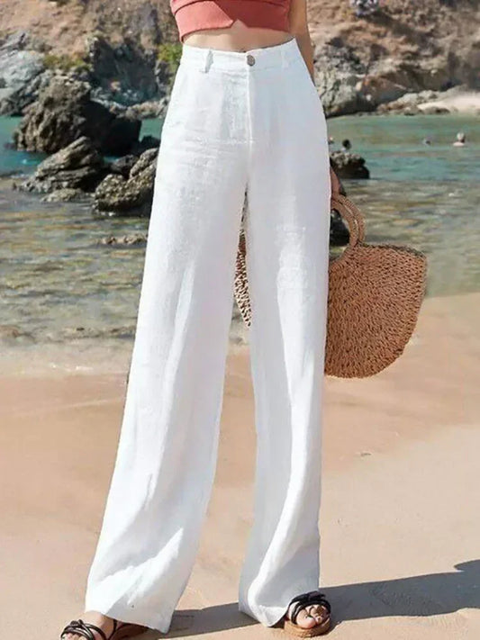 Person wearing white pants standing on  beach holding a wicker bag
