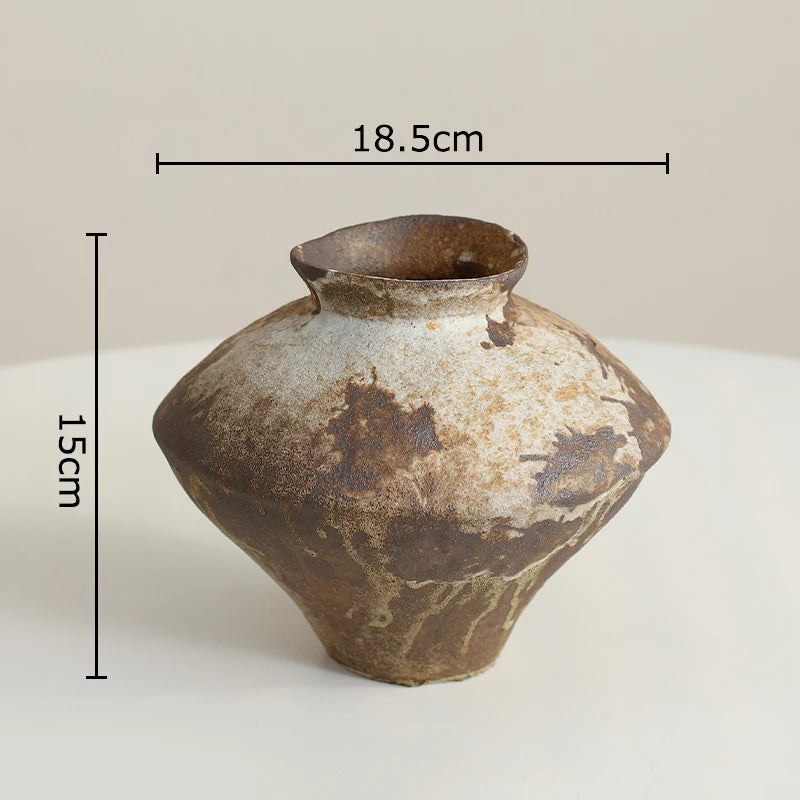A small handmade ceramic vase with a rustic, distressed glaze in brown and beige tones, shown with black dimension lines indicating a height of 15cm and a width of 18.5cm.