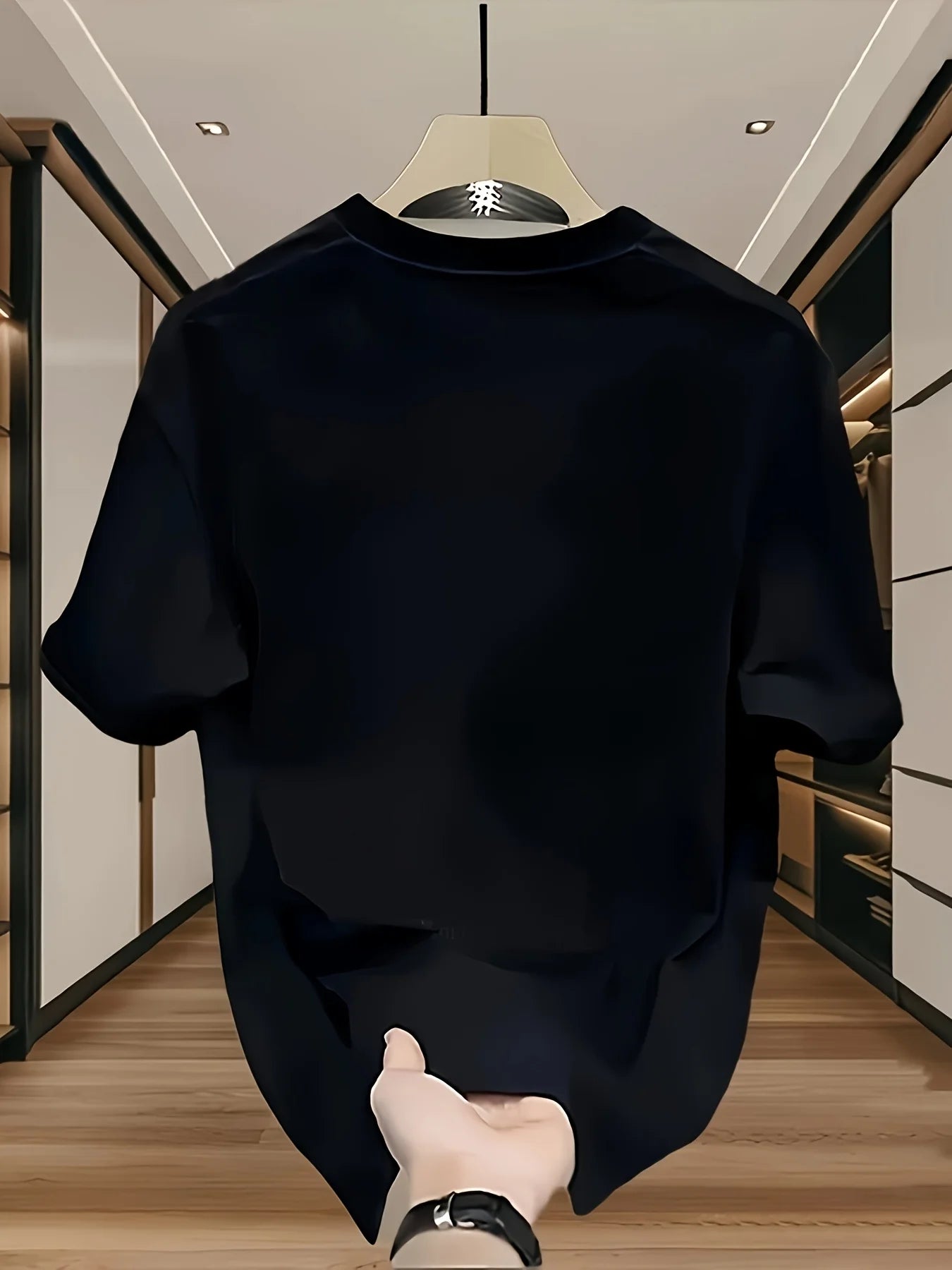 Black t-shirt on a hanger with a hand holding it, in a room setting.