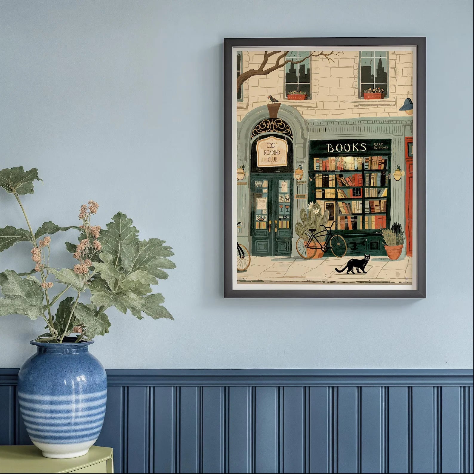 Framed artwork of a bookstore scene on a wall with a plant and vase below.