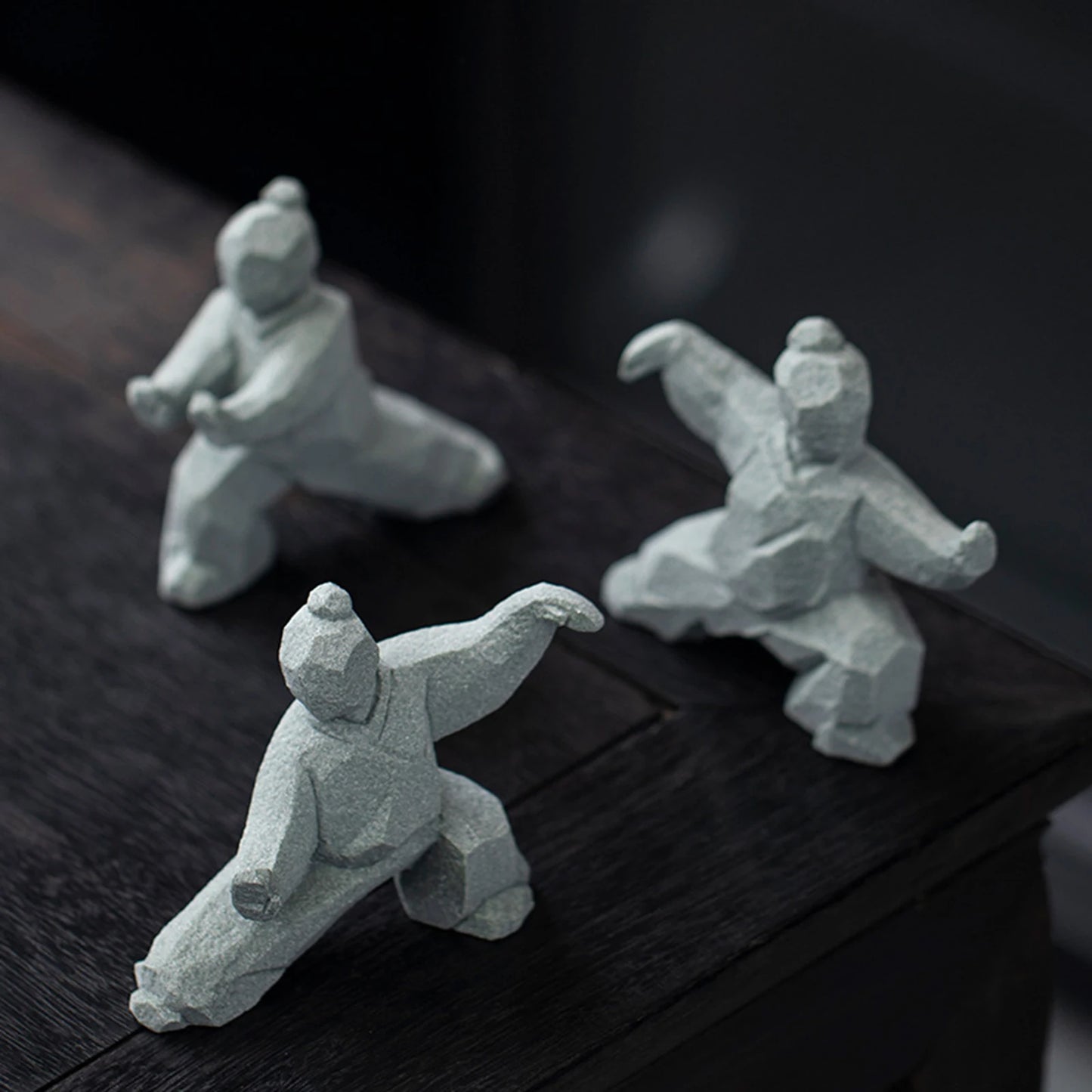 Three stone sculptures of martial artists on a dark wooden surface
