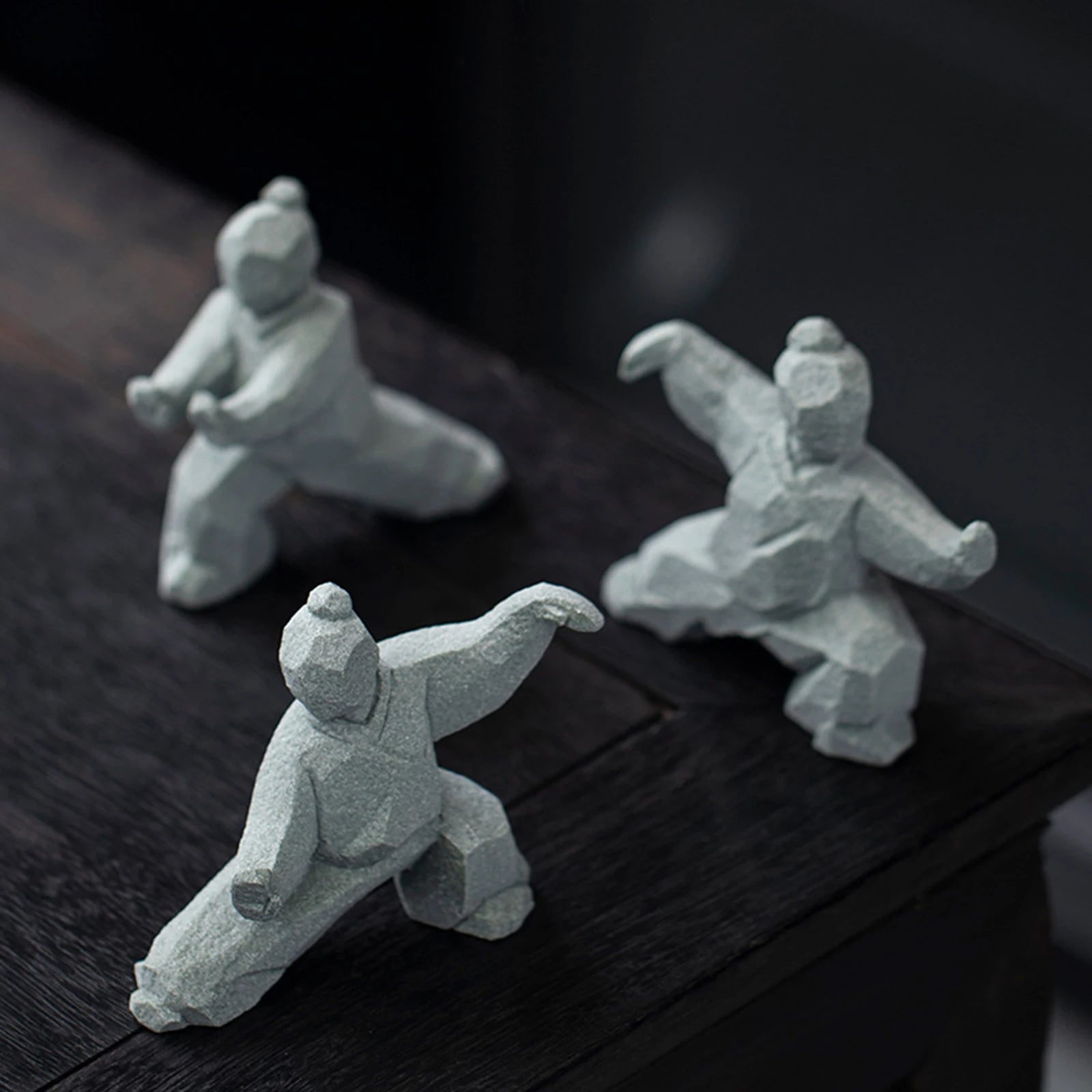 Three stone sculptures of martial artists on a dark wooden surface