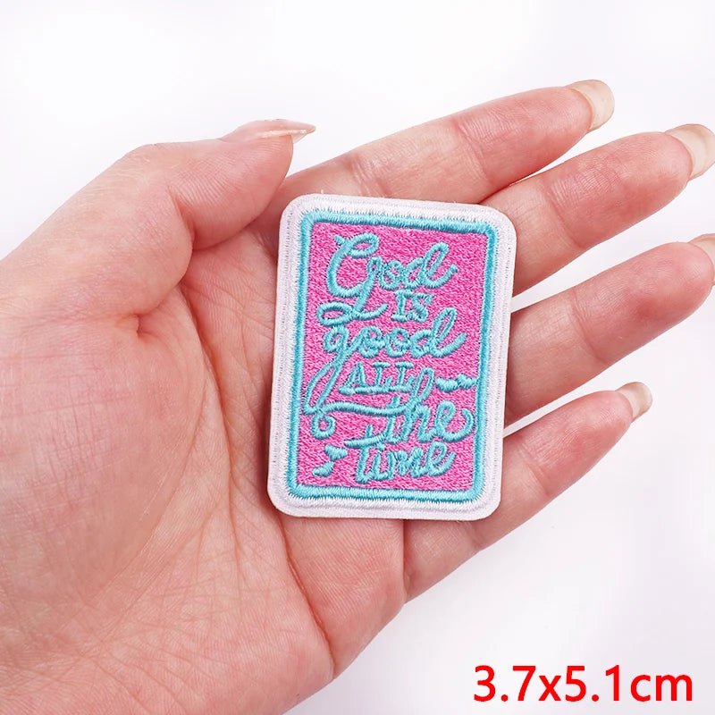 Embroidered patch with 'God is good all the time' text held in a hand on a white background
