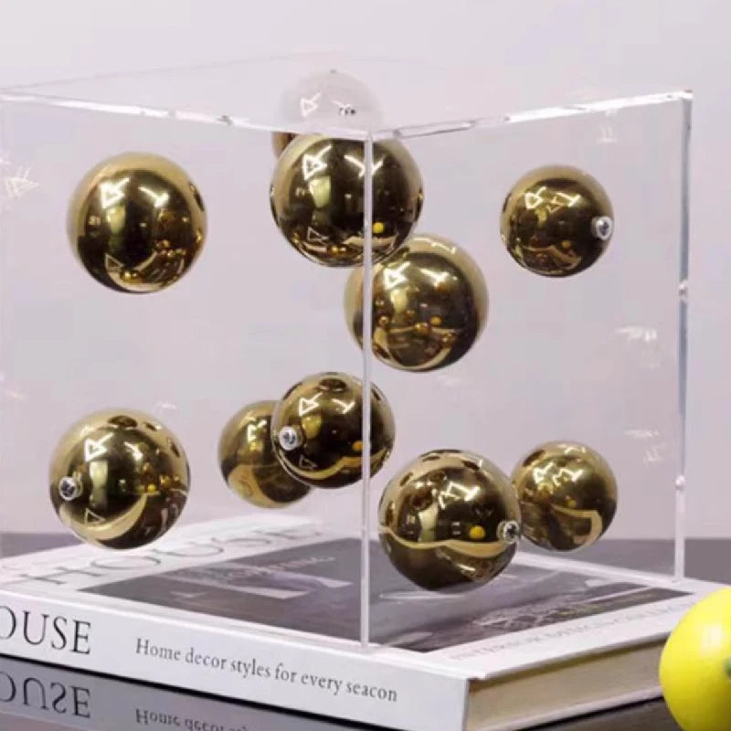 Gold decorative balls in a clear display case on top of books.