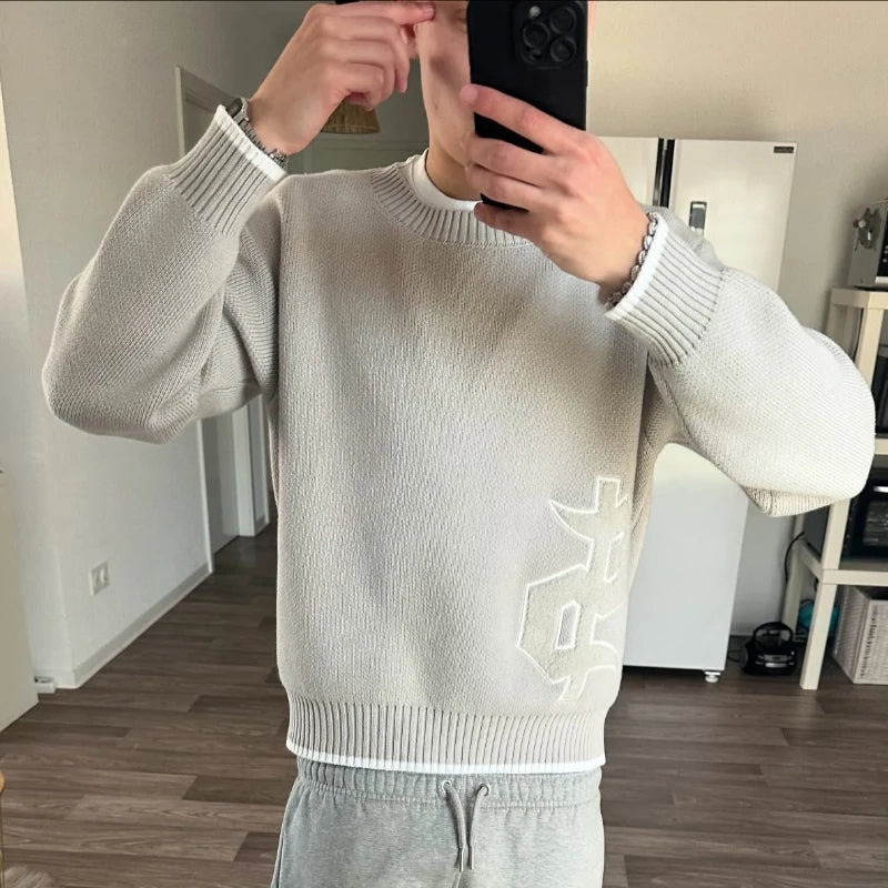 Person wearing a light gray sweater with a logo, taking a mirror selfie.