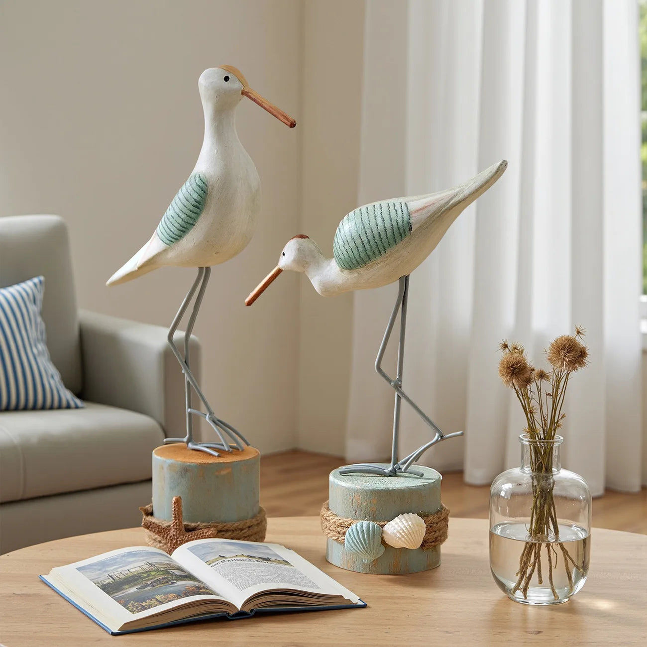 Two decorative bird figures on a table with an open book and a vase in the background.