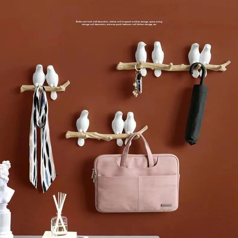 Decorative wall hooks with bird design holding a scarf, handbag, and umbrella on a brown wall.