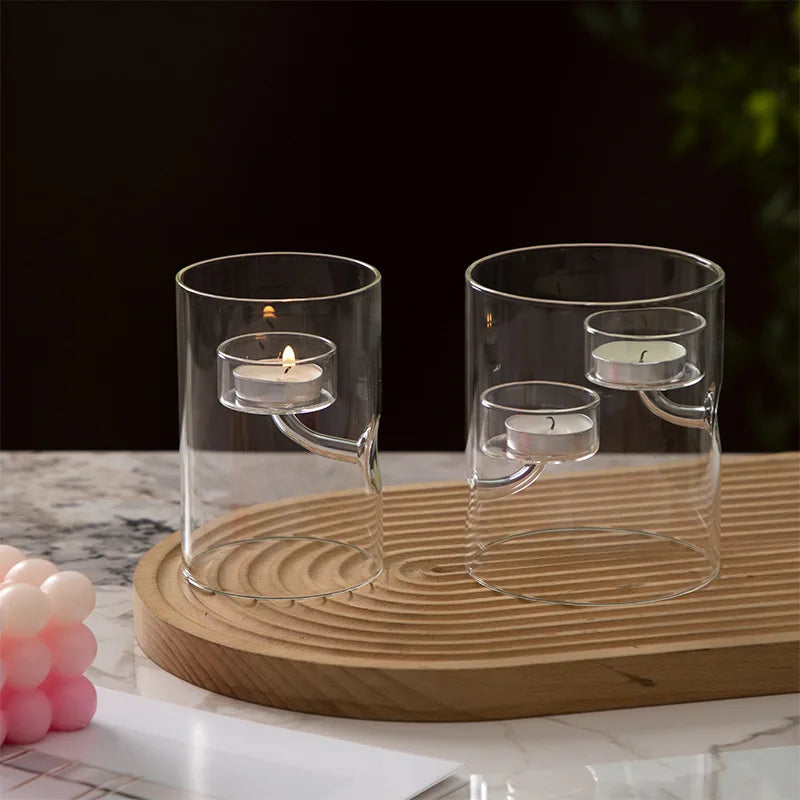 Two glass candle holders with candles on a wooden tray against a dark background
