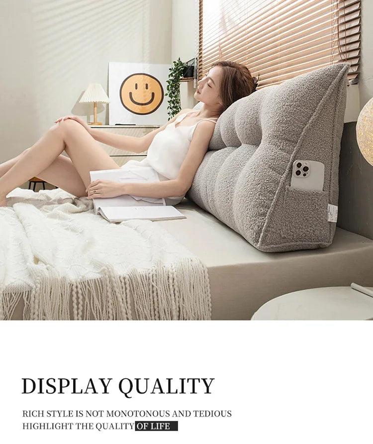 Woman lying on a bed with a wedge-shaped pillow, smiling at a computer screen.