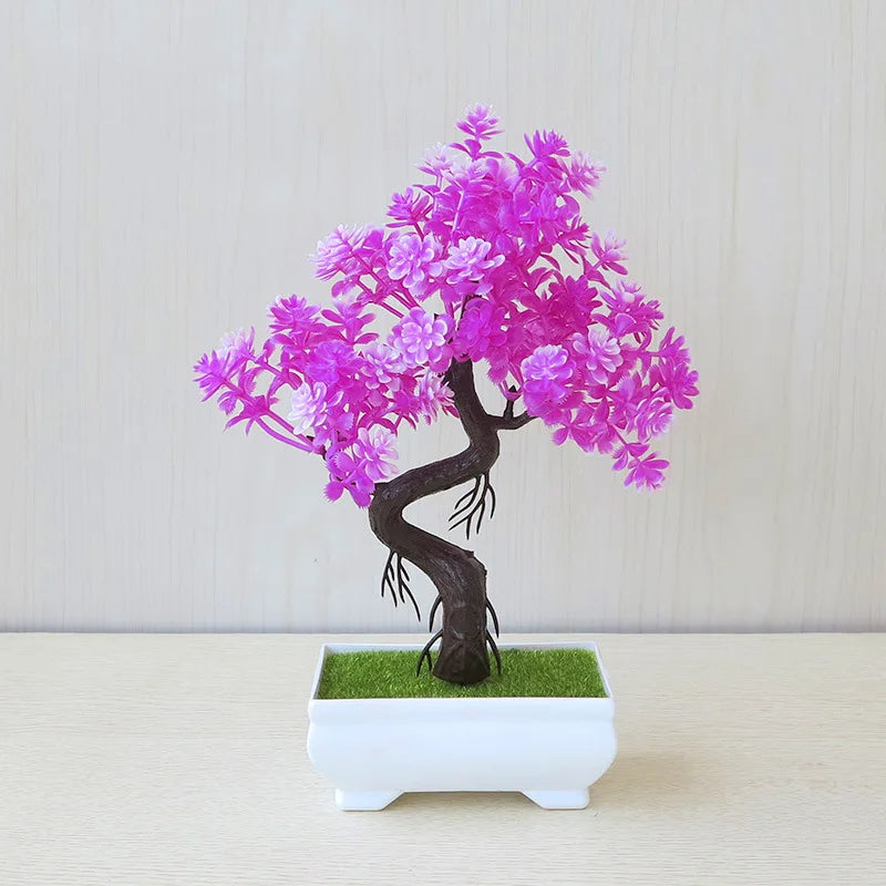 Bonsai tree with pink flowers in a white pot on a light wooden surface.