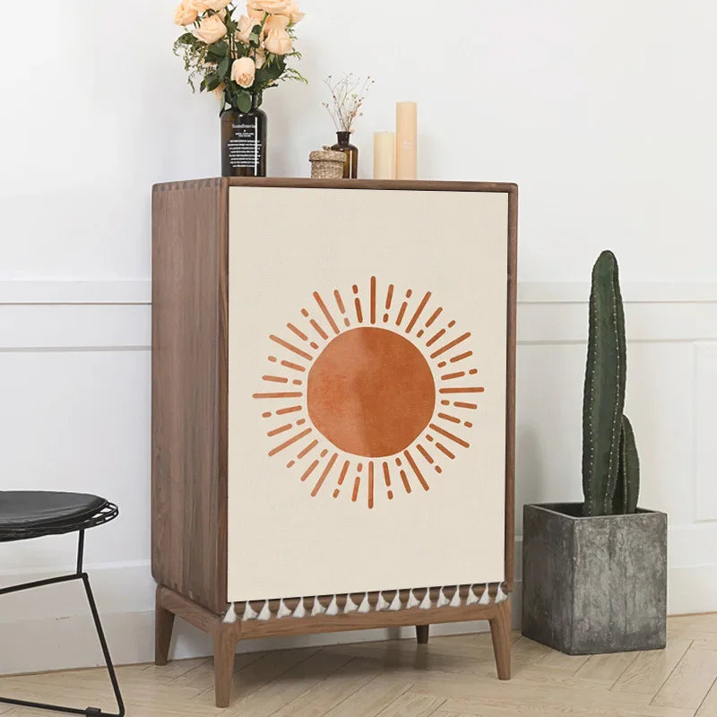 Wooden cabinet with sun design on a white wall, next to a cactus and flowers.