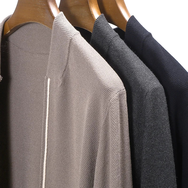 Three sweaters in gray, black, and beige on wooden hangers against a white background.