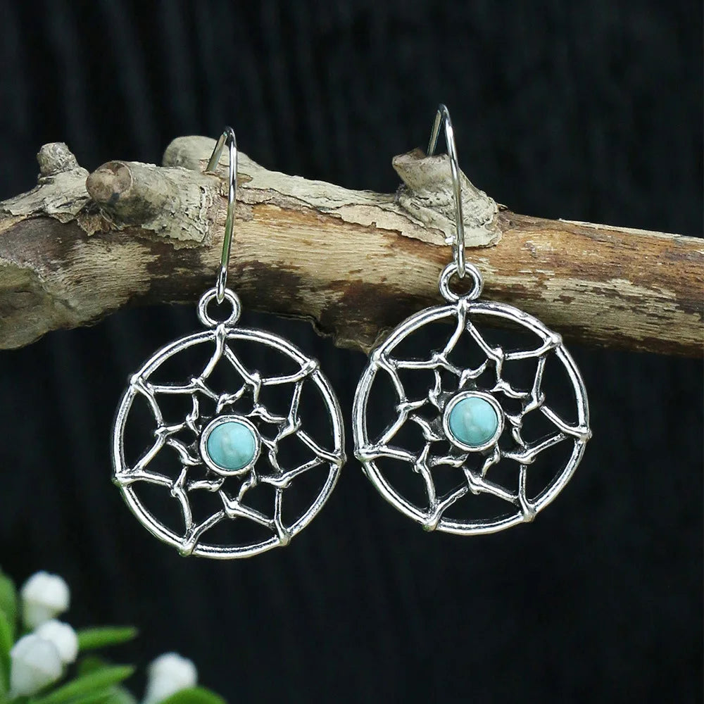 Silver earrings with turquoise stones on a wooden branch against a dark background