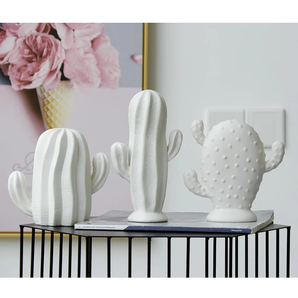 Three white ceramic cactus planters displayed on a black wire table in a styled interior setting.