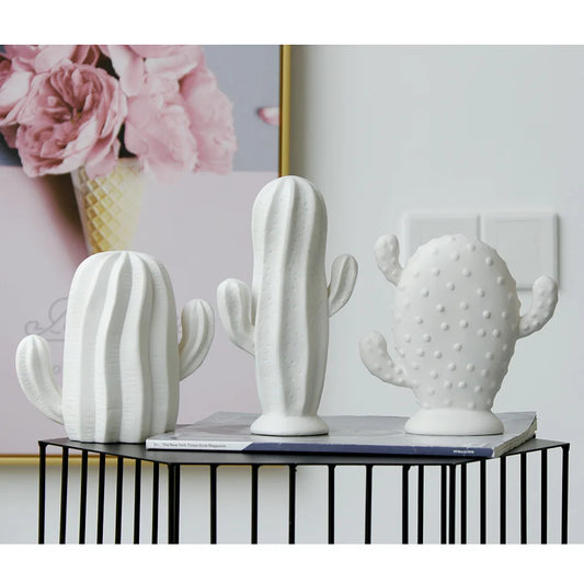 Three white ceramic cactus planters displayed on a black wire table in a styled interior setting.