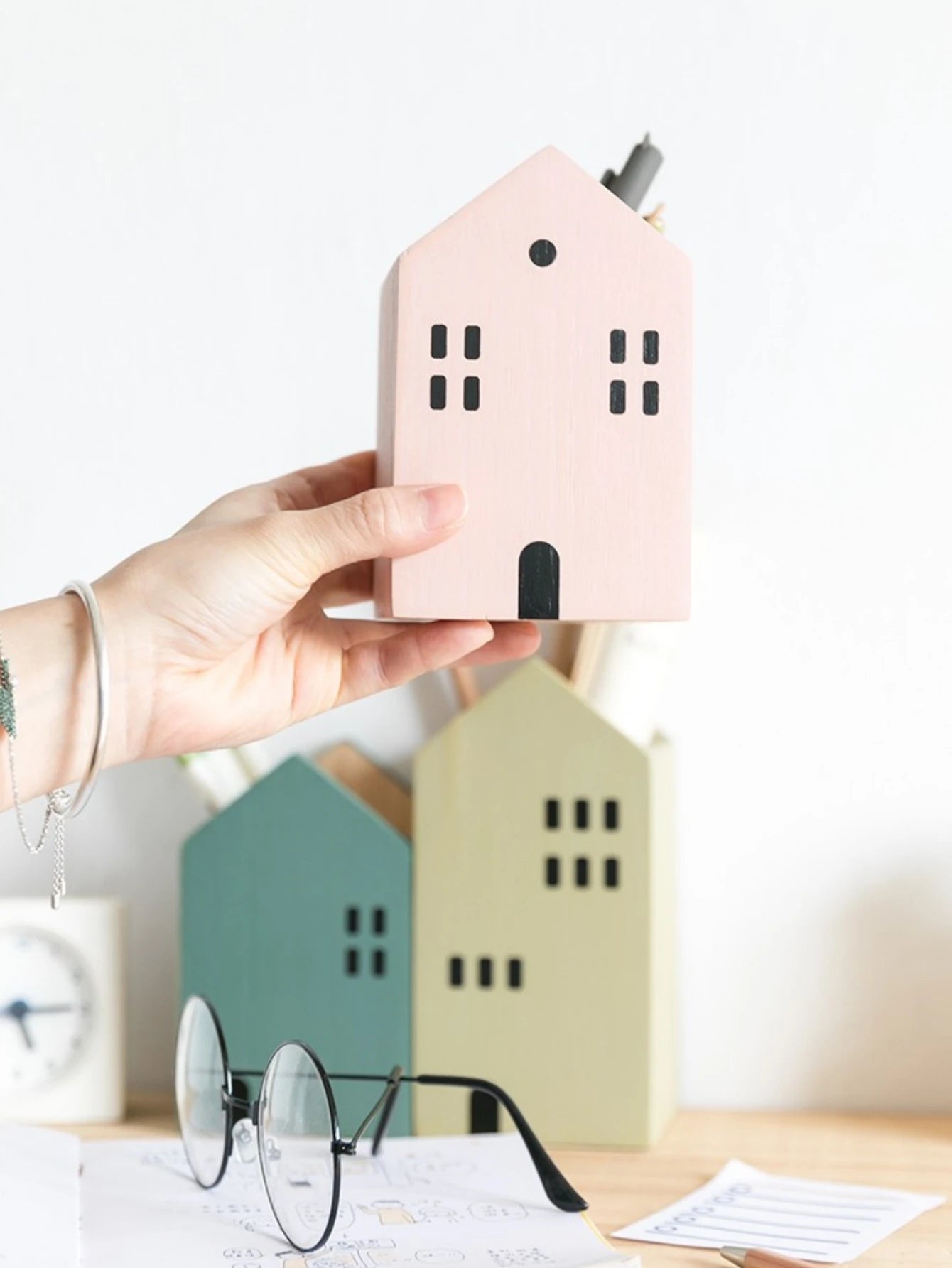 Hand holding a pink house-shaped object with more houses and glasses in the background