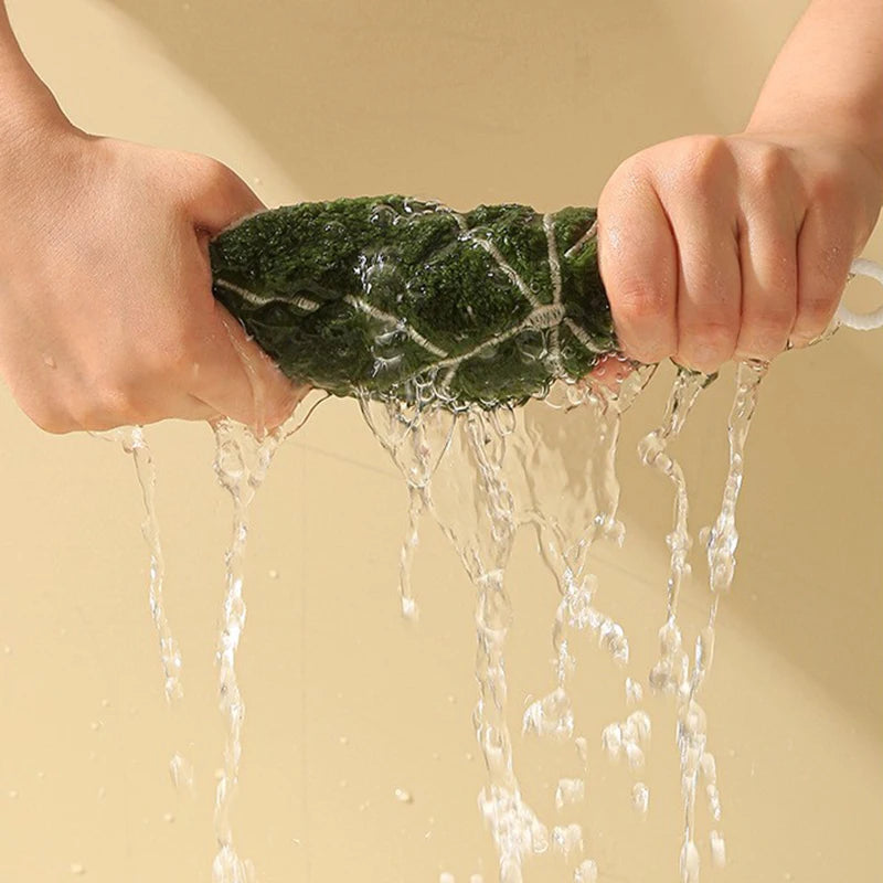 Person washing a green leaf hand towel under running water with a beige background