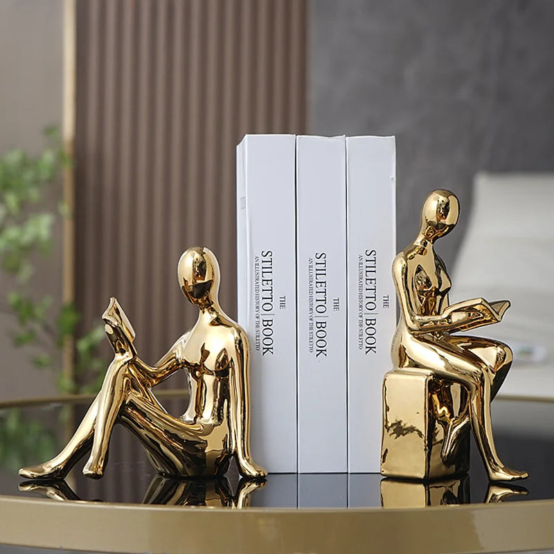 Gold human-like bookends on a stack of books with a blurred background