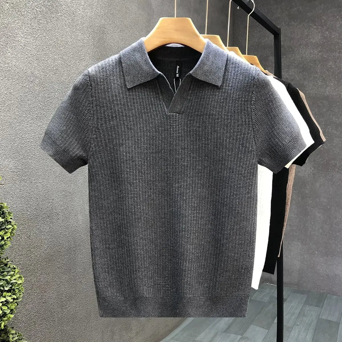 Gray polo shirt on a hanger against a gray wall