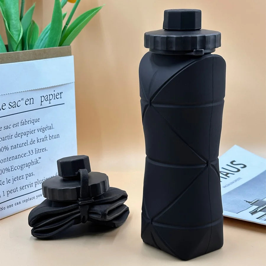 Black collapsible water bottle on a light brown surface with a plant and paper in the background