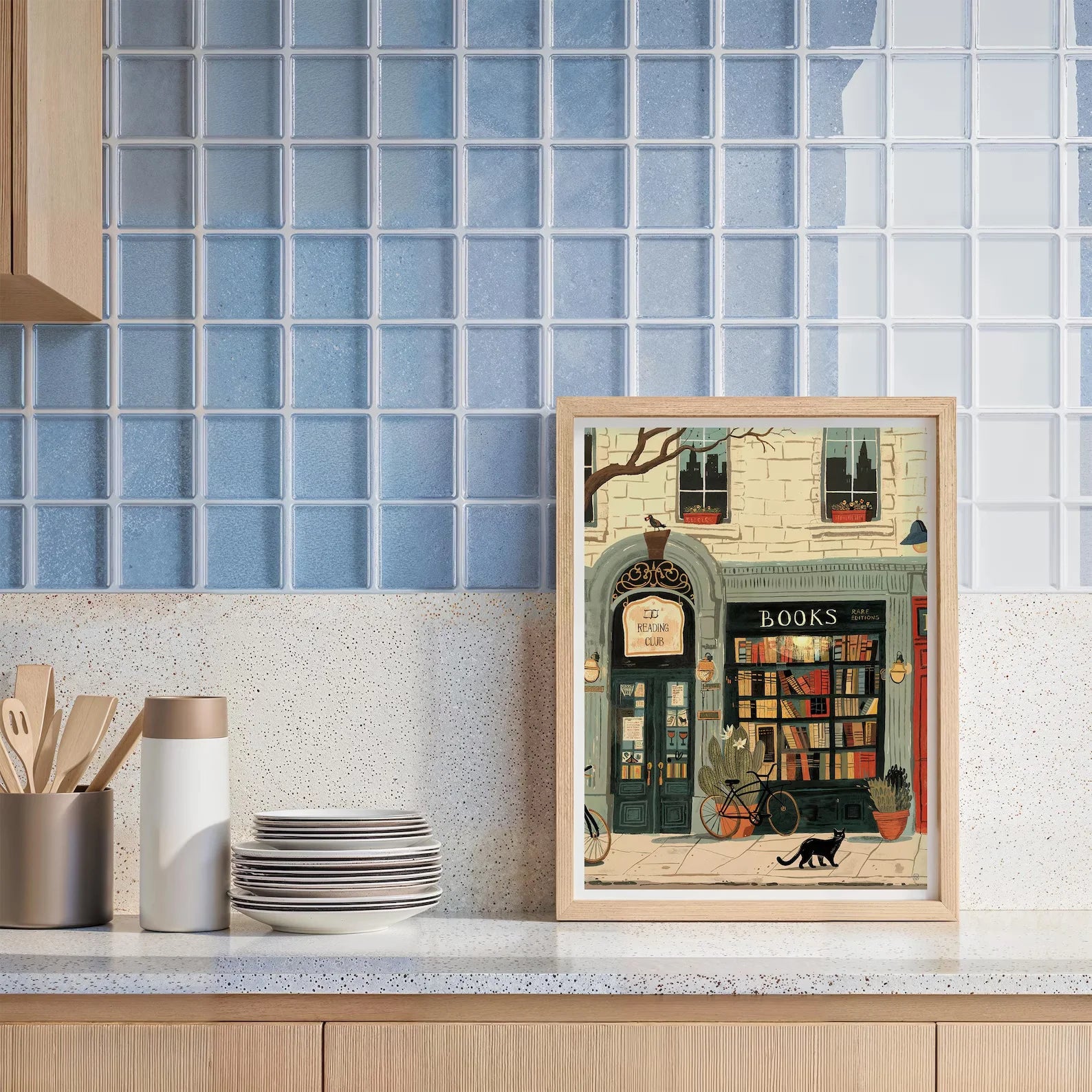 Framed artwork of a bookshop scene on a kitchen counter with blue tiled wall.