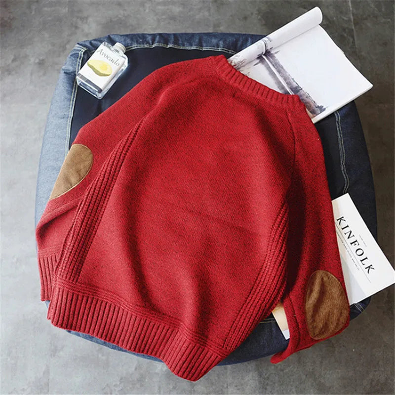 Red sweater with brown patches on a gray surface, with a KINFOLK tag visible.