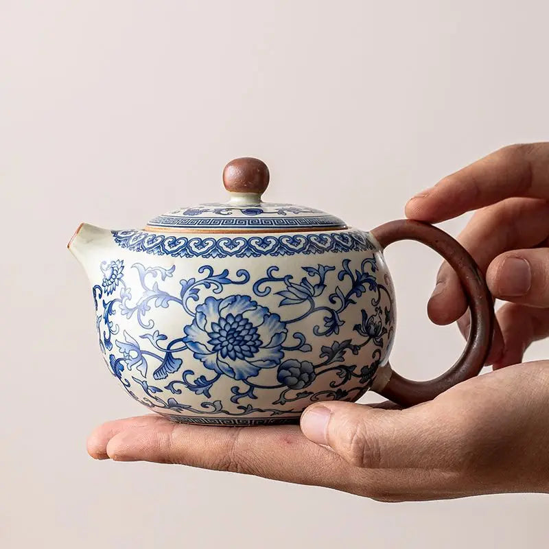 Ceramic teapot with blue floral patterns held by a hand against a neutral background