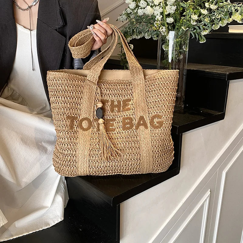 Woven tote bag with 'THE TOE BAG' text held by a person in an elegant setting.