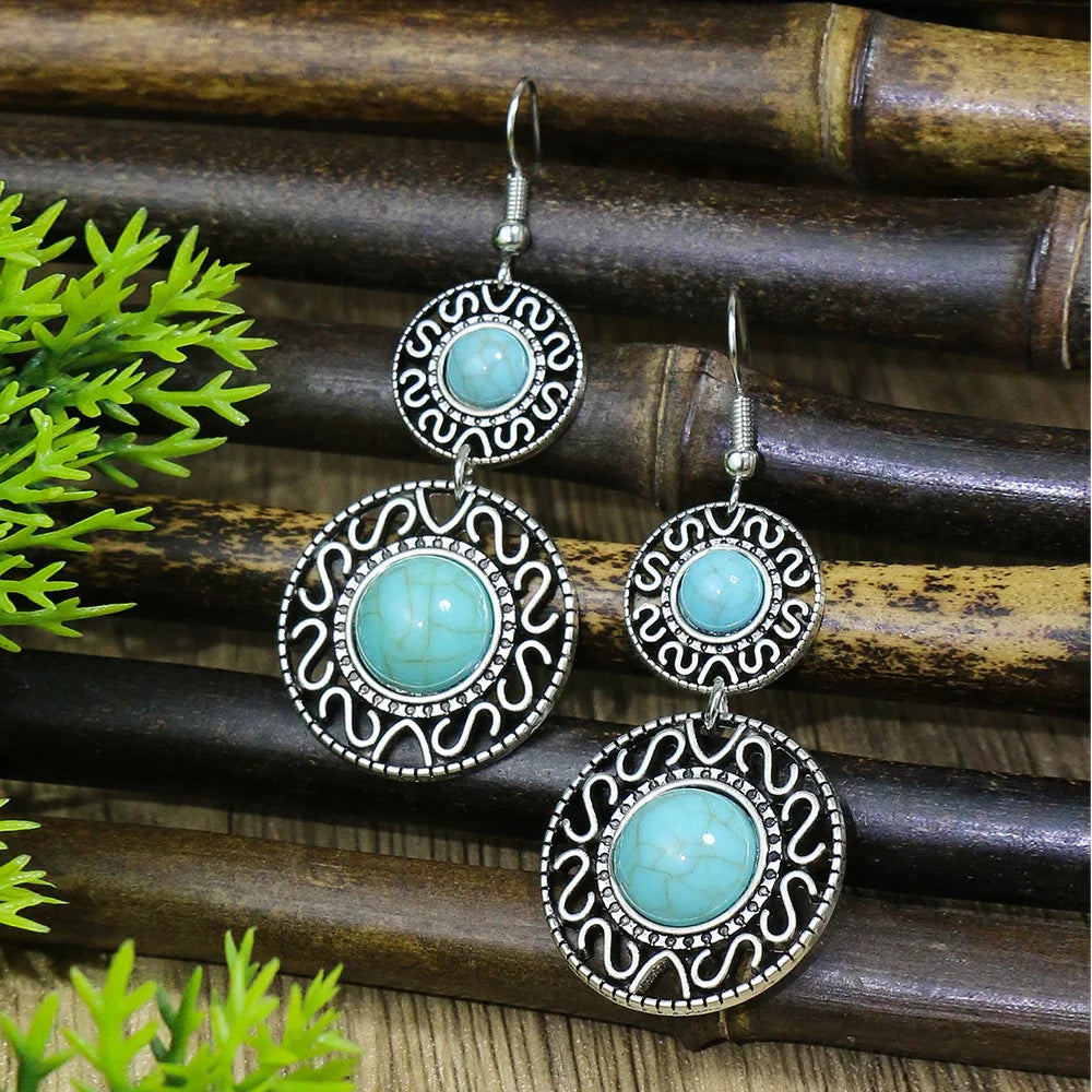 Turquoise earrings with silver intricate designs on a bamboo background