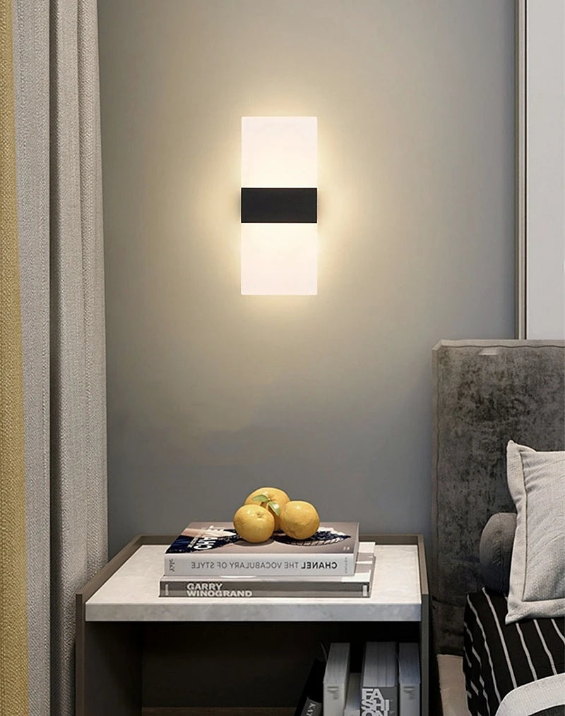 Modern wall sconce lighting fixture on a gray wall with a side table and books in the foreground.