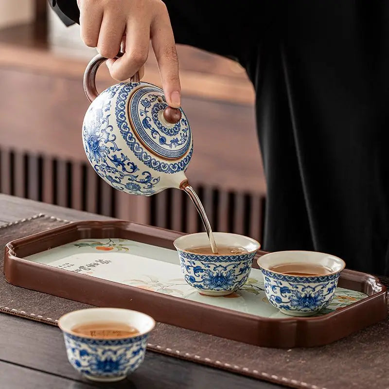 Person pouring tea from a blue and white teapot into two cups on a tray.