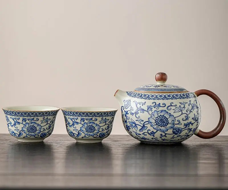 Ceramic teapot and two cups with blue floral patterns on a wooden surface.