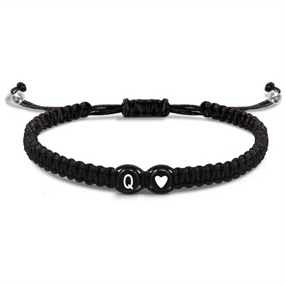 Black braided bracelet with letter 'Q' and heart charm on a white background