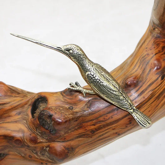 Bronze bird sculpture perched on a wooden branch against a white background