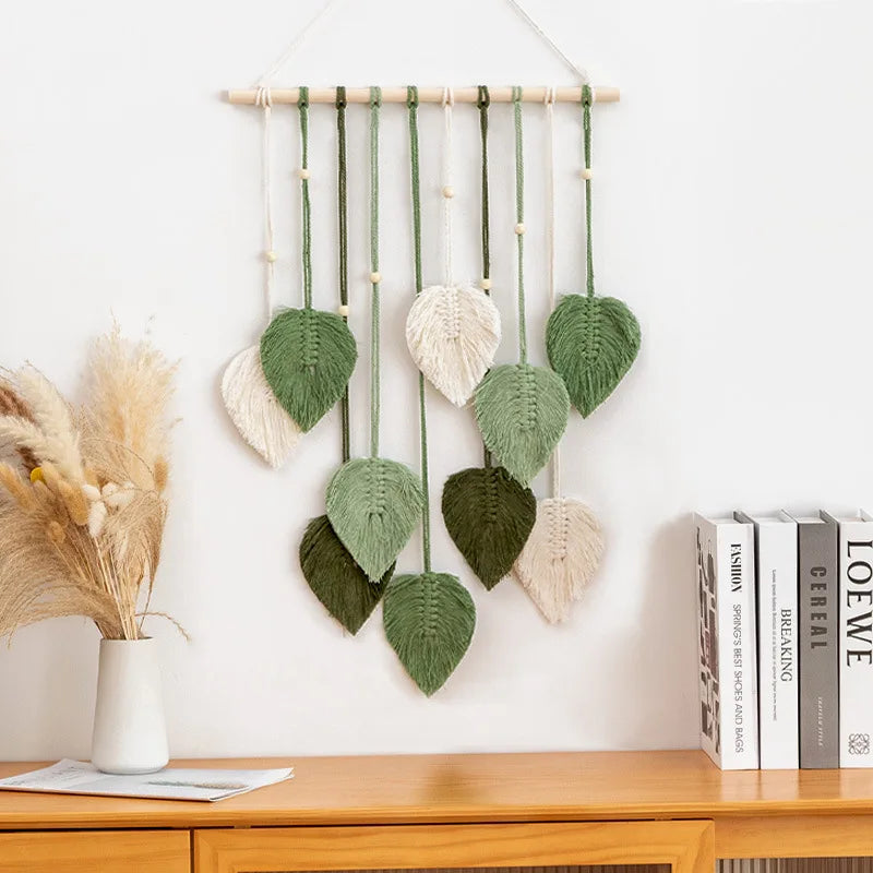 Green leaf macrame wall hanging tapestry with woven cotton leaves and wooden rod in boho home interior