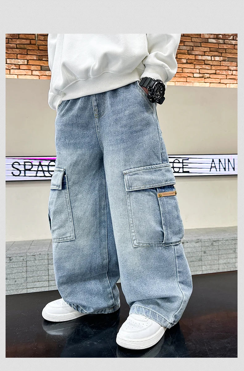 Person wearing light blue cargo pants with a white sweatshirt and black gloves in front of a brick wall.