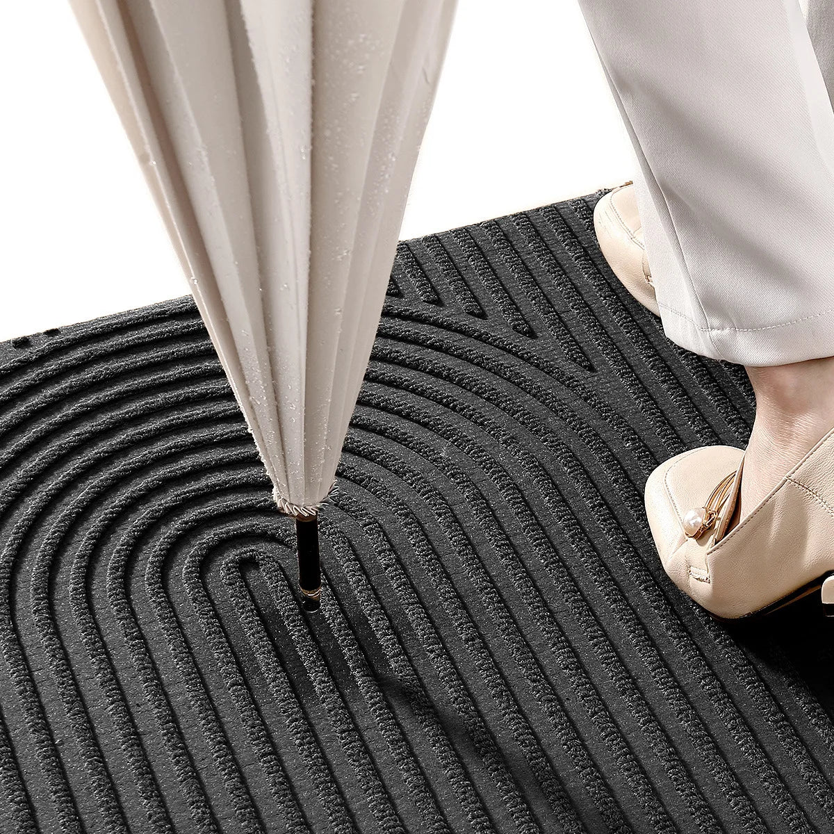 Person holding an umbrella on a textured black mat with white pants and shoes.