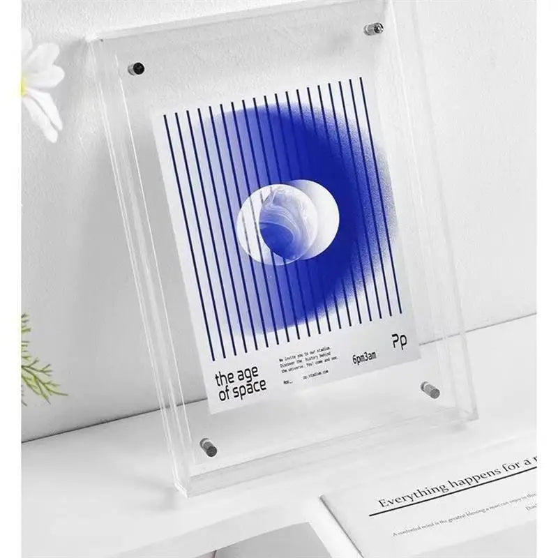 A clear acrylic display frame holding a blue and white art print with vertical stripes and a circular design, photographed on a white shelf against a light wall.
