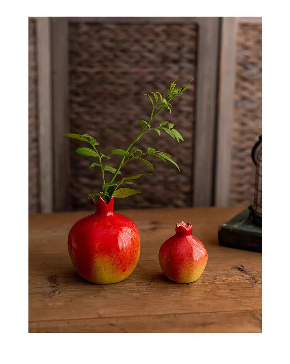 Two ceramic pomegranate-shaped vases with green leaves on a wooden surface.