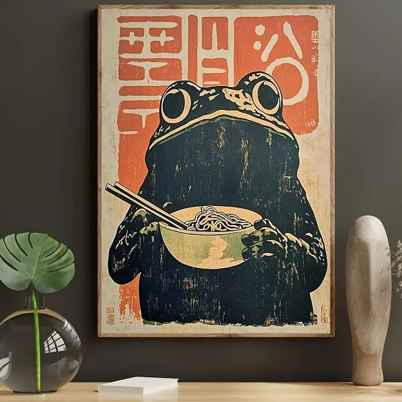 Framed artwork of a frog eating noodles with chopsticks on a dark wall.