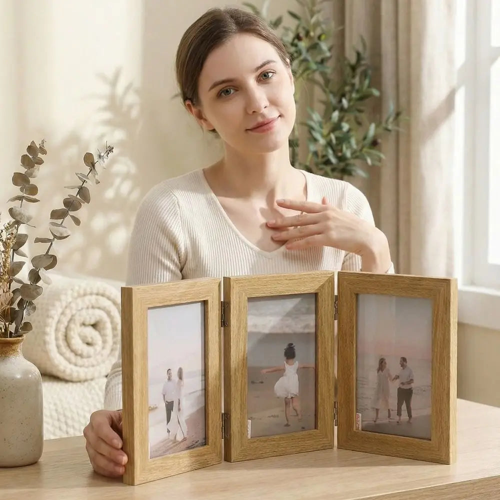 A woman sits at a wooden table holding a three-frame wooden photo collage. The frames display photos of a couple walking on a beach.