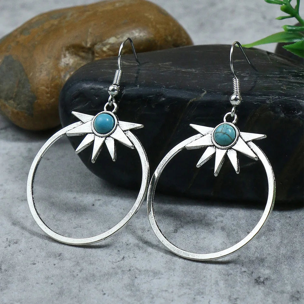 Silver hoop earrings with turquoise stones on a stone surface