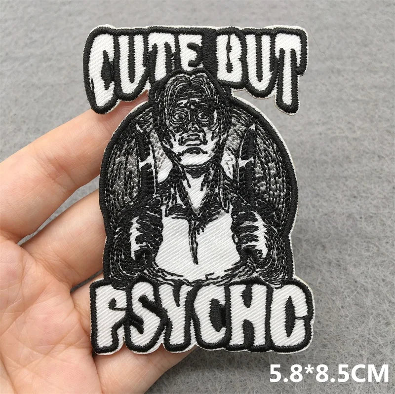 Embroidered patch with a character and 'Cute But Psychic' text held by a hand on a gray background.