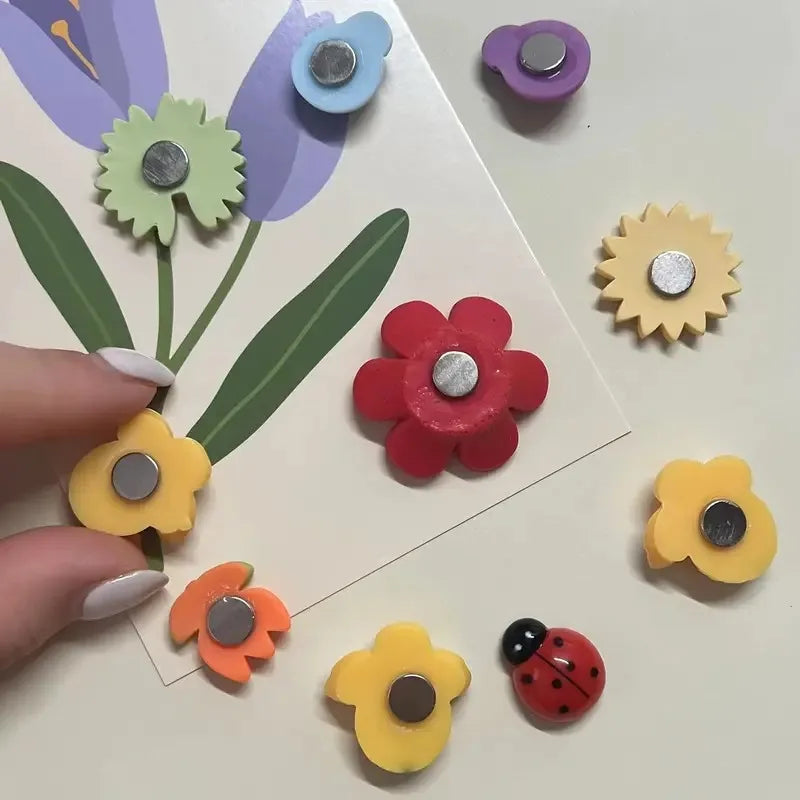Colorful flower-shaped magnets on a white surface with a hand holding one of them.