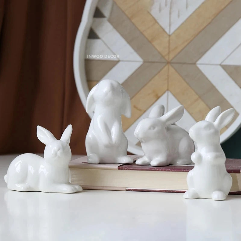 Four white ceramic rabbit figurines on a surface with a decorative wall in the background.