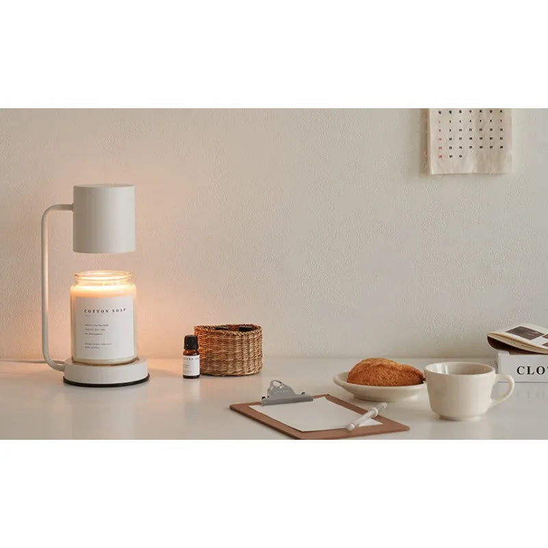 Candle with a diffuser on a table next to a mug, pastry, and other items.