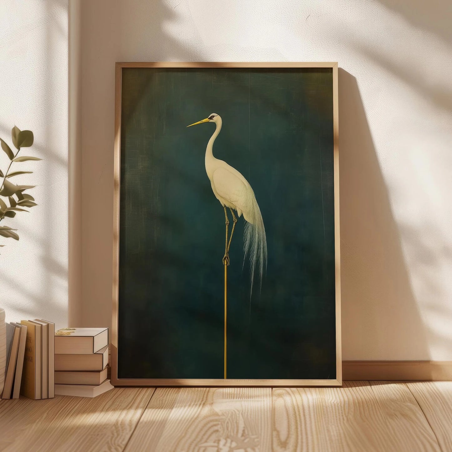 Framed artwork of a crane on a dark green background in a room with wooden floor and books.