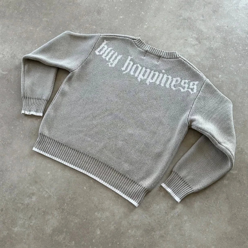 Gray sweater with 'buy happiness' text on a concrete floor