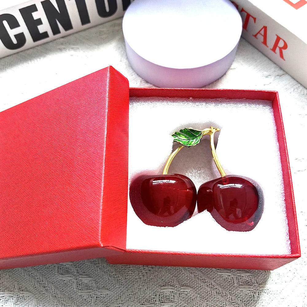 Red cherry ornaments with gold accents in a red box on a textured surface.