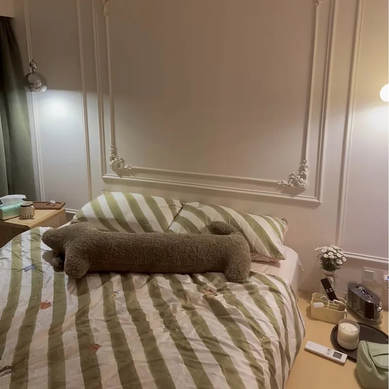 dachshund-shaped cushion on a bed featuring striped bedding and a large mirror on the wall.